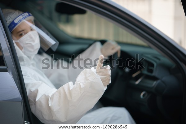 Woman driver\
with gloves,protective hazmat suit, face shield and mask.\
corona\
virus or Covid-19\
protection.
