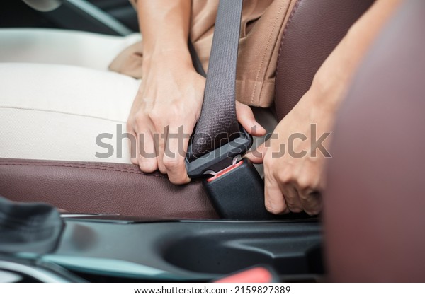 woman driver hand fastening seat belt during\
sitting inside a car and driving in the road. safety, trip, journey\
and transport concept