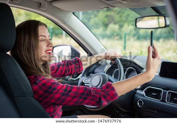 Woman driver is holding a smartphone\
on her hand while sittinf in front driver seats in\
car.