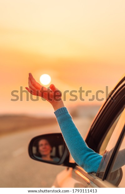 Woman\
driver putting hand out of car window while driving in warm autumn\
sunset, enjoying the ride and feeling the\
wind