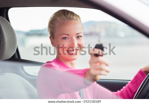 Woman driver\
showing car keys. Young female driving happy about her new car or\
drivers license. Caucasian\
model.