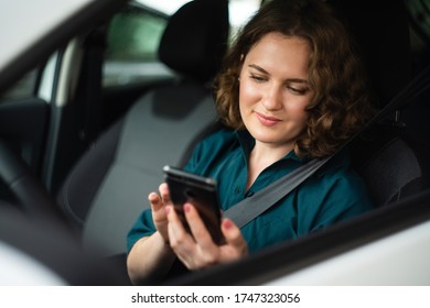 Woman driver sitting in car and looking at smartphone screen