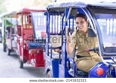 Woman driver sitting in e rickshaw and showing thumbs up gesture
