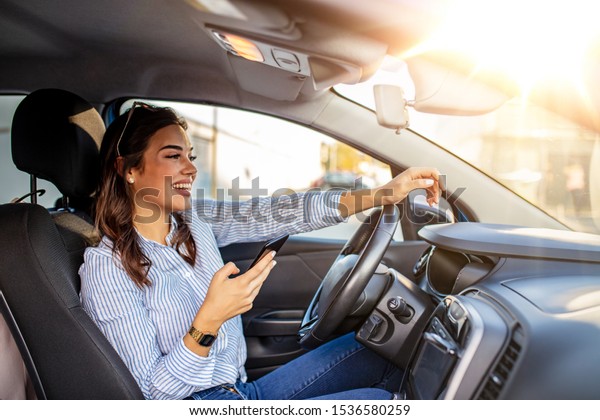 Woman driver\
using a smart phone in car. Woman driver using a smart phone in\
car. Leisure, road trip, technology, travel and people concept -\
Happy woman driving car with\
smarhphone