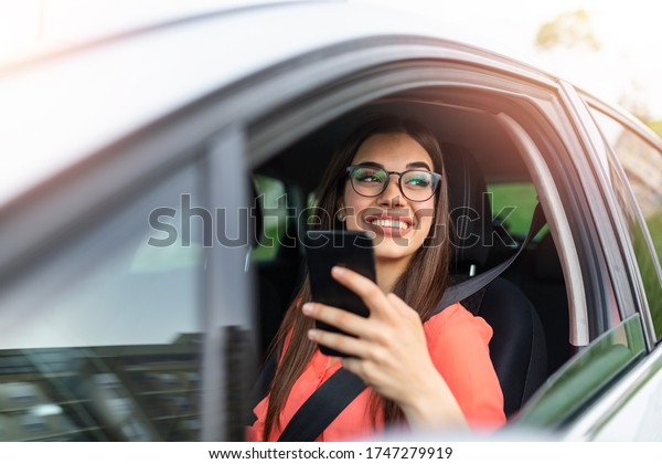 Woman driver\
using a smart phone in car. Woman driver using a smart phone in\
car. Leisure, road trip, technology, travel and people concept -\
Happy woman driving car with\
smartphone