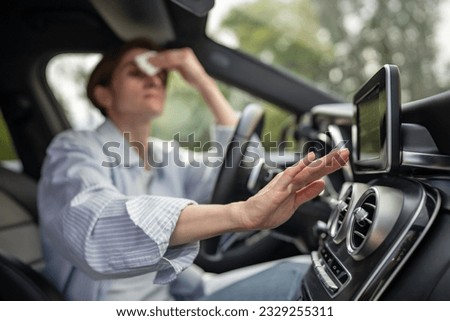 Woman drives car with broken air conditioning in hot summer weather wipes sweat on forehead with paper napkin. Middle aged female suffering from heat stuffiness. Exhausted overheated stressed driver.