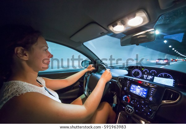 Woman drives car in\
illuminated tunnel.