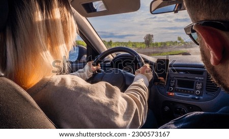 A woman drives a car with an instructor on a sunny summer day. View from the back of the car. A woman learns to drive a car against the backdrop of a beautiful rural landscape.