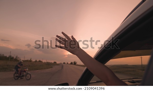 Woman drives car sticking out hand at sunset\
in countryside