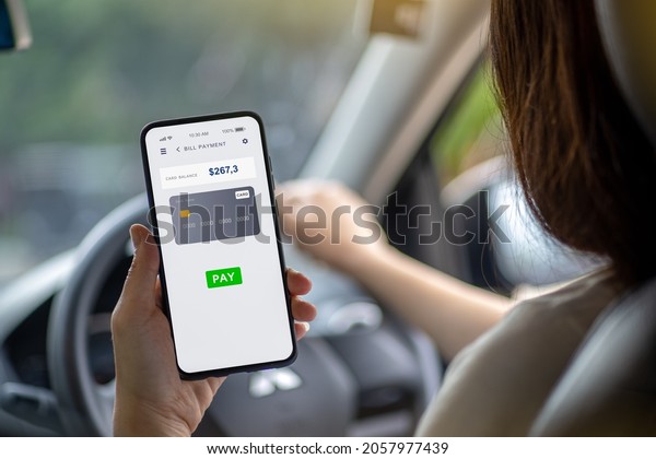 A woman driving a black car and use the phone to\
pay bills with applications via credit card. Smartphone technology\
concept.