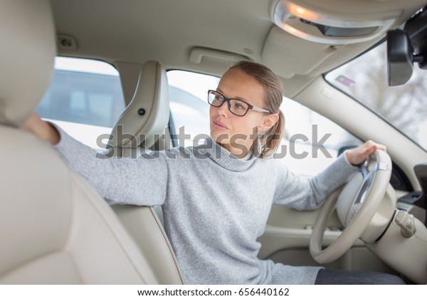 Woman driving a car - female driver at a wheel of
a modern car, parking, going in reverse using the parking sensors
(DOF; color toned image)