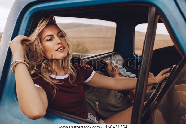 Woman driving a\
car with friends sleeping on a road trip. Group of females going on\
a long drive in a car.