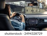 Woman driving a car, hands on the wheel close-up, view from the back to the road.