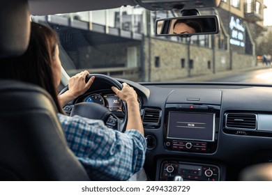 Woman driving a car, hands on the wheel close-up, view from the back to the road.