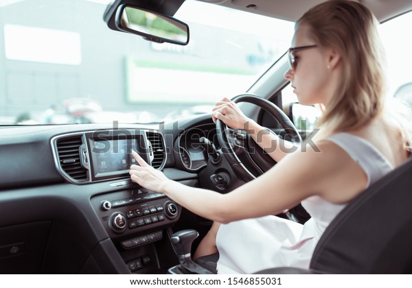 woman driving car, presses
finger on touch screen, selects application on Internet, activates
radio navigation and searches for route in the city. Background
parking mall