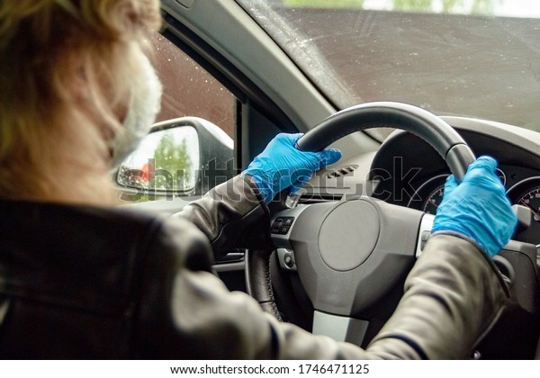 A\
woman is driving a car in protective gloves. Taxi driver. Driving a\
car during quarantine. Blue gloves. Protective mask. Protective\
gloves. Virus protection. Protection against\
bacteria.