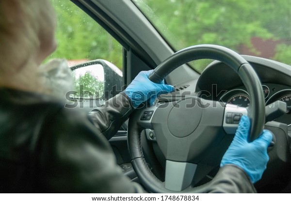 A\
woman is driving a car in protective gloves. Taxi driver. Driving a\
car during quarantine. Blue gloves. Protective mask. Protective\
gloves. Virus protection. Protection against\
bacteria.