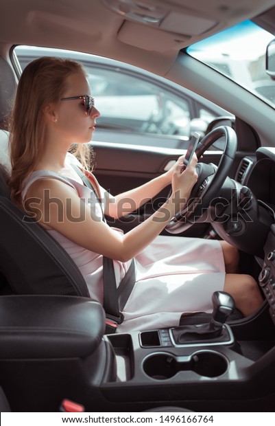 A woman driving car, sitting in mobile phone,\
writing message in parking lot near shopping center, waiting for\
friends, online application on Internet, long waiting for her\
husband at store