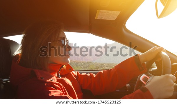 Woman driving a car.\
Young woman is driving a car on a sunny day. Confident woman in\
sunglasses driving car. Woman in a red jacket driving with Lens\
optical flare