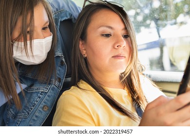 Woman Driving Checking Her Cell Phone While Her Daughter With A Mask Looks At Her