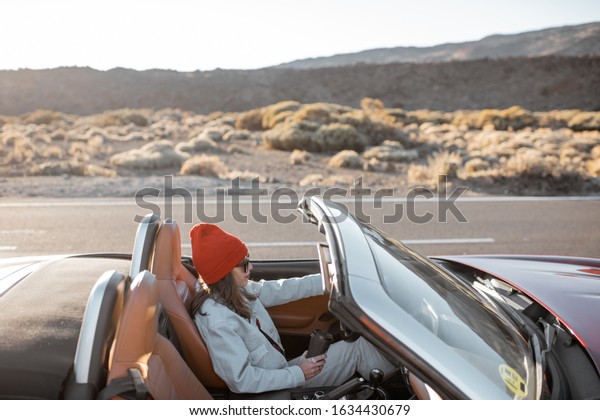 Woman\
driving convertible car while traveling on the desert road during a\
sunset. Carefree lifestyle and travel\
concept