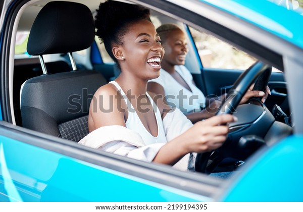 Woman driving, friends and roadtrip for a fun and\
happy drive while enjoying their vacation, trip and journey\
together. Black women laughing and talking while sitting in car for\
an adventure or lift