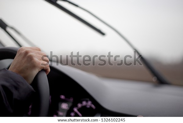 A woman driving her car in rainy weather and
having to turn on the wipers.