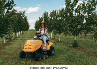 Woman Driving Lawn Mower In Orchard