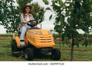 Woman Driving Lawn Mower In Orchard