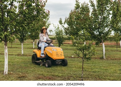 Woman Driving Lawn Mower In Orchard