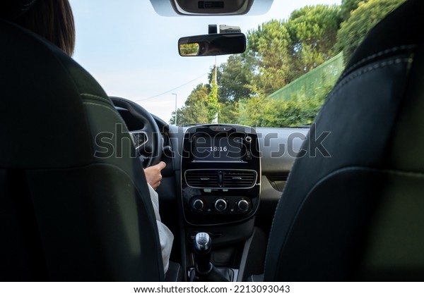 Woman Driving, view from the\
back seat at a low angle to the car main dashboard with screen\
clock with 18:16 time showing. From the back rear passenger seat\
POV.