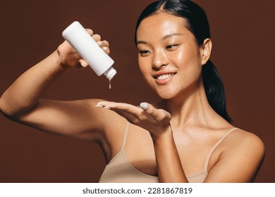 Woman dropping face serum on her hand in the midst of her skincare routine. Young woman smiling as she applies a beauty treatment, which moisturizes and nourishes the skin for a radiant, flawless look - Shutterstock ID 2281867819