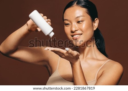 Woman dropping face serum on her hand in the midst of her skincare routine. Young woman smiling as she applies a beauty treatment, which moisturizes and nourishes the skin for a radiant, flawless look