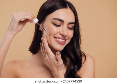 Woman Dropping Serum on Face on Beige Background. European Girl Applying Serum Collagen Moisturizer from Pipette on Face close up. Positive Laughing Beauty Woman Portrait. Concept of Face Skin Care - Powered by Shutterstock