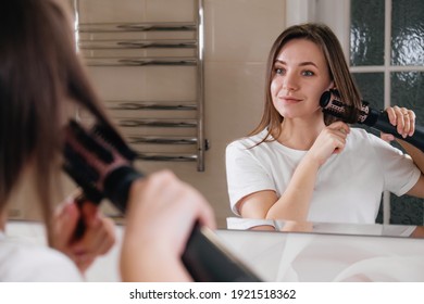 Woman Drying Her Hair, Styling In The Bathroom Near Mirror