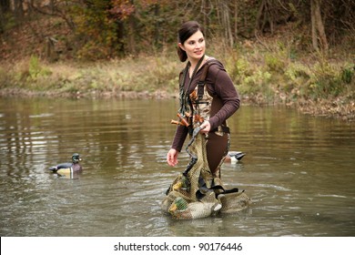 Woman Duck Hunter in Camo Waders in Pond with Decoys Bag