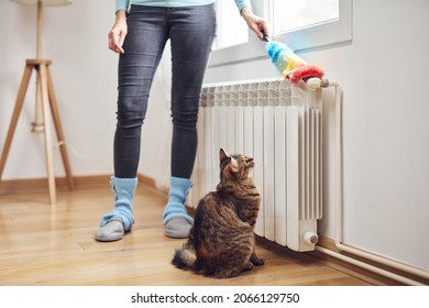 Woman With A Dust Stick Cleaning Central Heating Gas Radiator At Home.