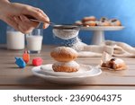Woman dusting powdered sugar onto delicious Hanukkah donuts on wooden table, closeup