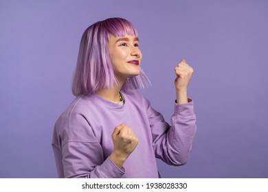 Woman With Dyed Purple Hair Is Very Glad And Happy, She Shows Yes Gesture Of Victory, She Achieved Result, Goals. Surprised Excited Happy Lady On Violet Studio Background. Jackpot Concept.