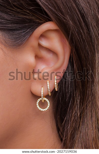 Woman ear with mulriple\
piercings wearing beautiful earrings with zirconia- details\
capture