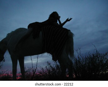 A woman in the early evening gestures from the top of her horse.