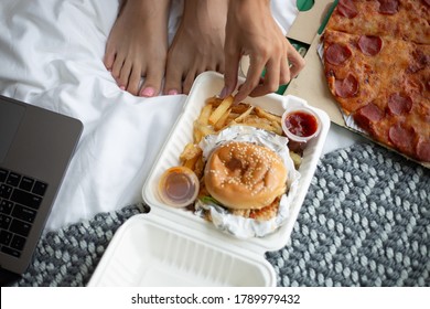Woman East Fast Food From Delivery On Bed In Bedroom At Home. Female Enjoying Fat Food, Pizza And Burgers.  Hungry For Carbs. 