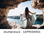 Woman in eastern dance dress standing in beautiful sea cave. Traveling. Summer holidays. Woman with long dark hair and beautiful blue long dress on the edge by the sea of Cyprus