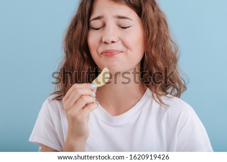 woman eat slice of lime, make grimaces, in studio, isolated on blue background, copy space, close up