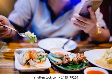 Woman is eating along with playing smartphone. Lifestyle in today's society. woman relaxing having  in the diner and watching some funny videos by smartphone while eating food. lady playing games. - Powered by Shutterstock