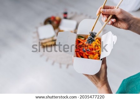 Woman eating asian chinese food noodles with vegetables in wok box using chopsticks. Food delivery. Take away lunch
