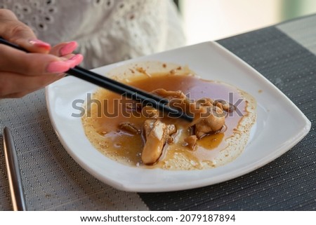 Woman is eating a Asian dish with chicken and Teriyaki sauce with chopsticks at the restaurant