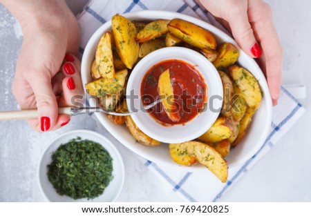 woman is eating baked potato slices with herbs in a white dish with tomato sauce, light background, top view. Vegan Healthy Food Concept.