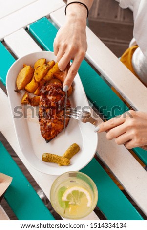 Woman is eating bbq chicken breast with baked jacket potatoes on summer terrace