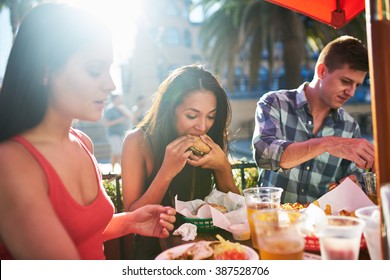 Woman Eating Big Burger Together With Friends At Outdoor Restaurant